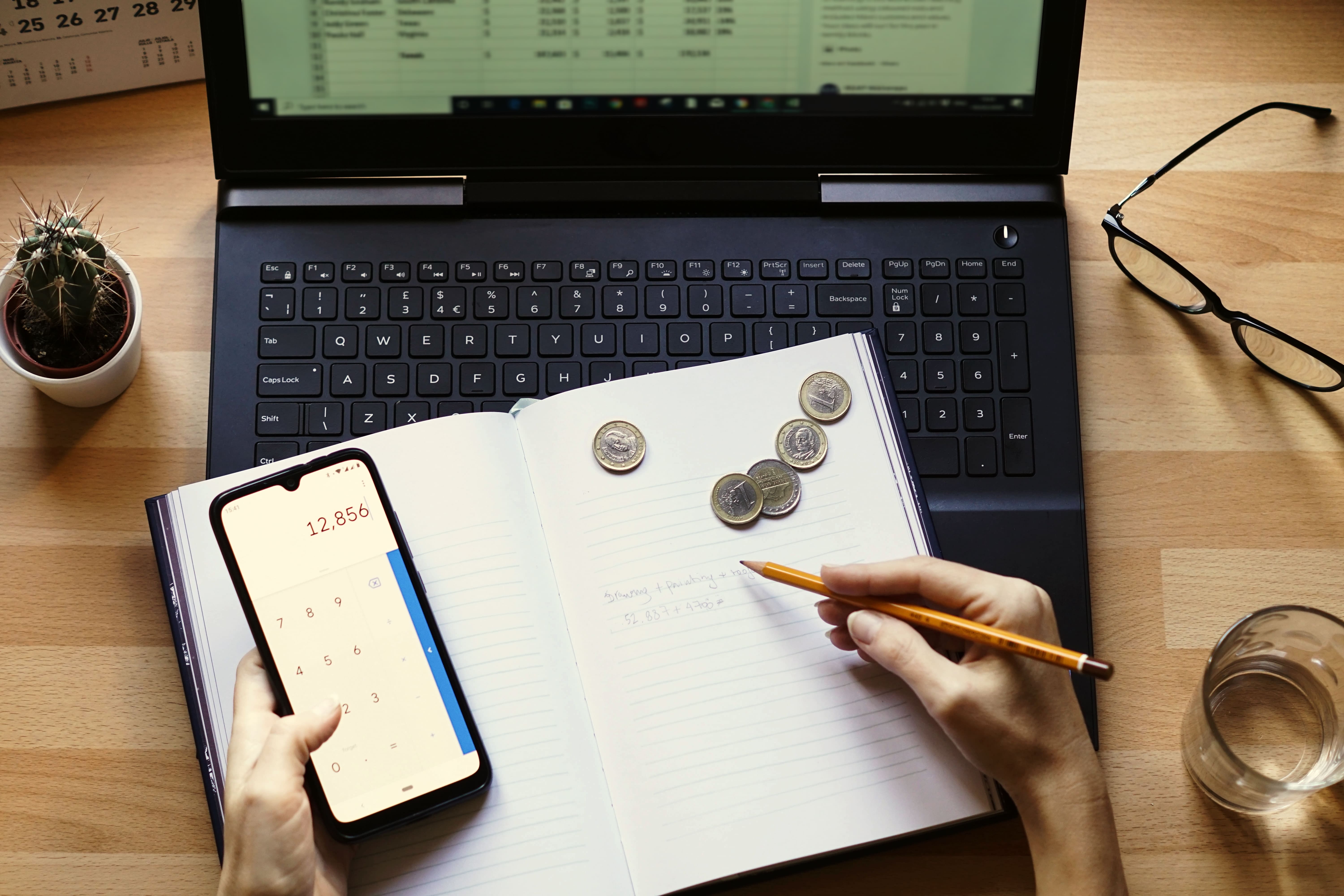 Person calculating finances with smartphone and notebook on desk — custom software for petty cash 				tracking in SMEs.
